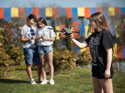 Noia amb un dron a la mà i dos joves al fons