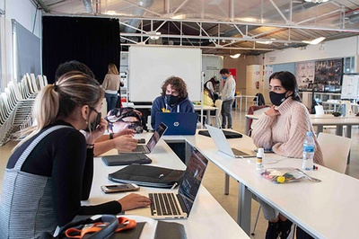 Estudiants asseguts a una taula amb ordinadors, treballant