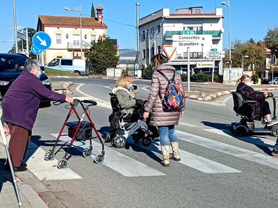 Un grupo de voluntarios con silla de ruedas cruzando una calle en Lliçà d'Amunt