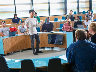 Estudiante hablando en un aula rodeado de otros estudiantes