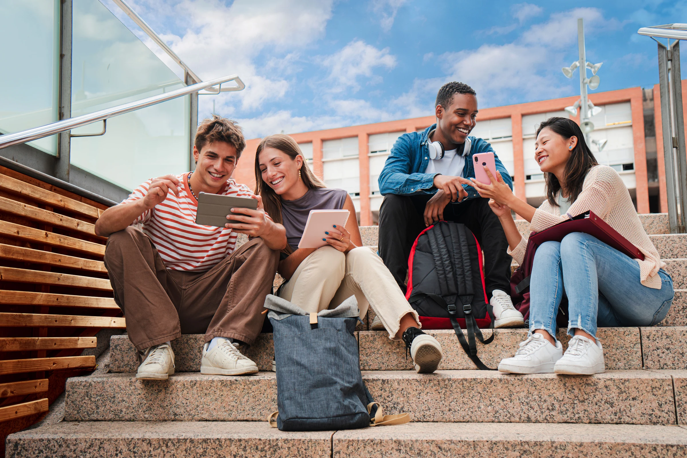 Cuatro jóvenes comentando los contenidos de un móvil y una 'tablet' sentados en unas escaleras del Campus Diagonal Nord de la UPC.